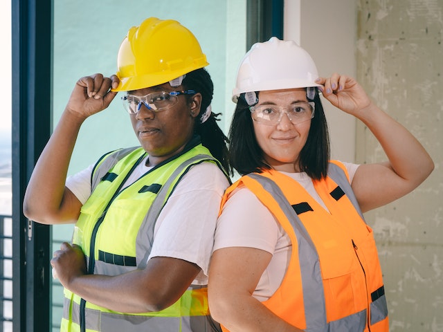 two people with hard hats and high visibility vests standing back to back